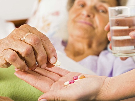 A caregiver gives a female patient medicine with a glass of water