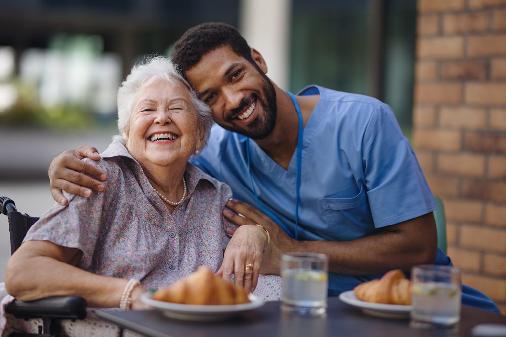 Skilled nursing in elder care: a caregiver has breakfast with a smiling, elderly woman.
