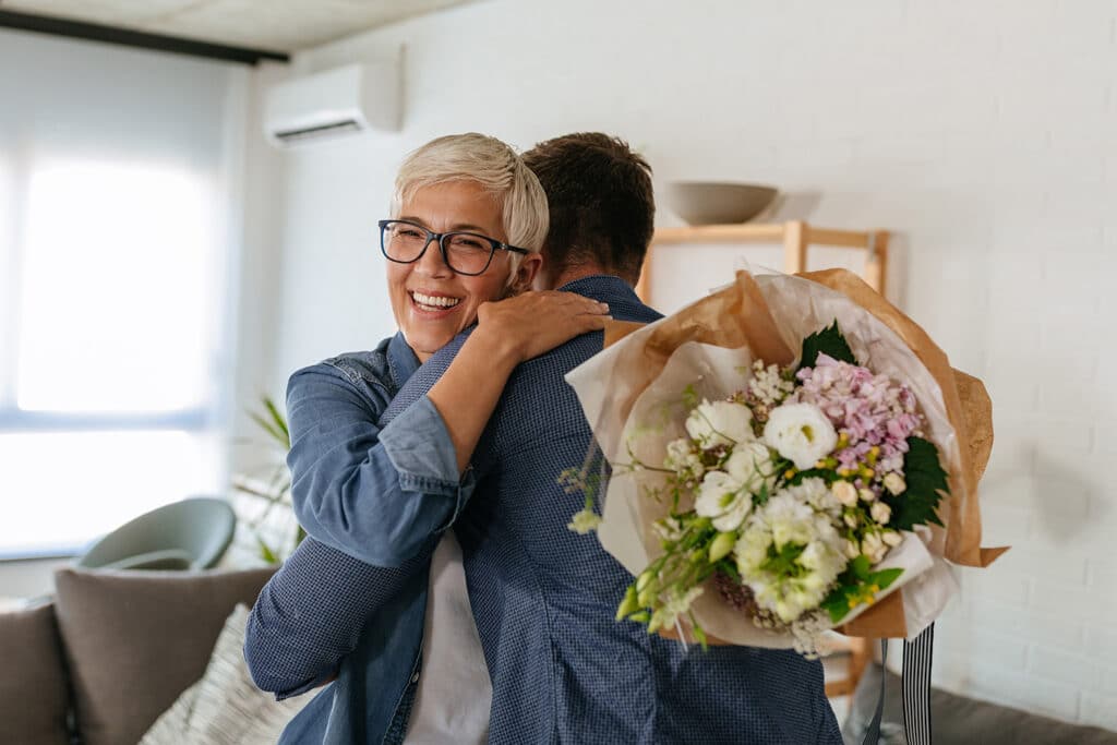 A senior woman holding a bouquet of flowers and hugging a younger man.